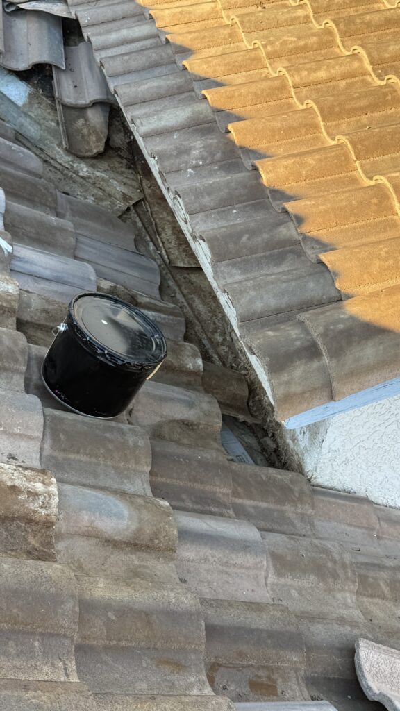 Displaced roof tiles and debris beside a stucco wall, with a black work bucket