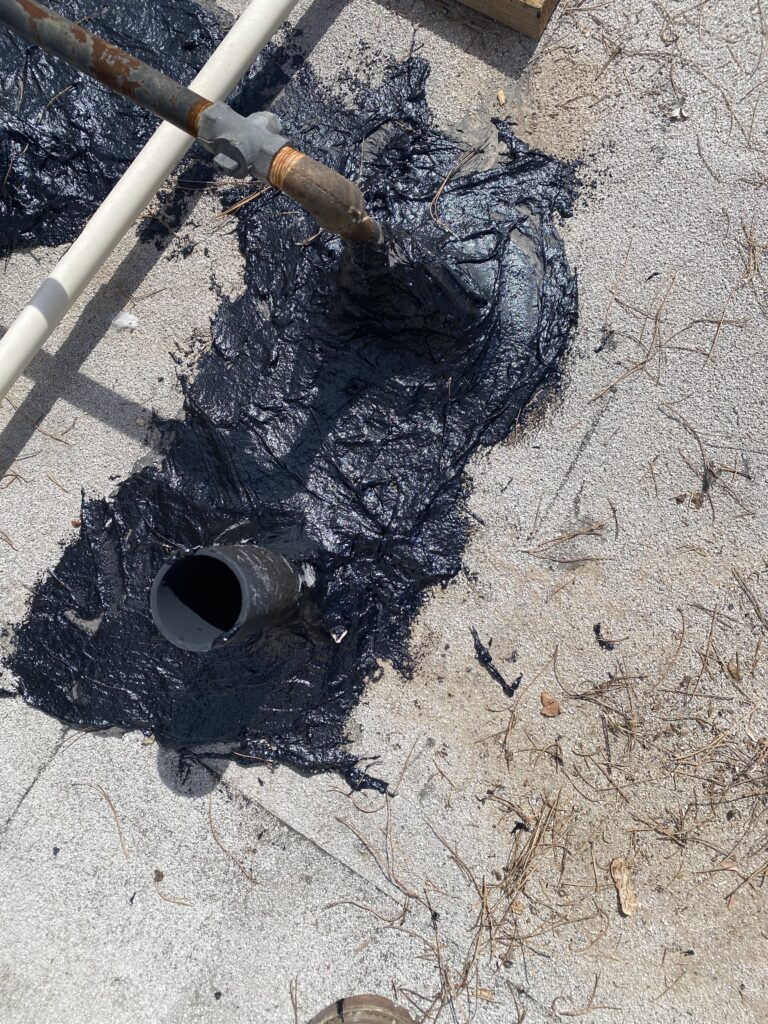 Close-up of rooftop pipe penetrations surrounded by black sealant and scattered pine needles