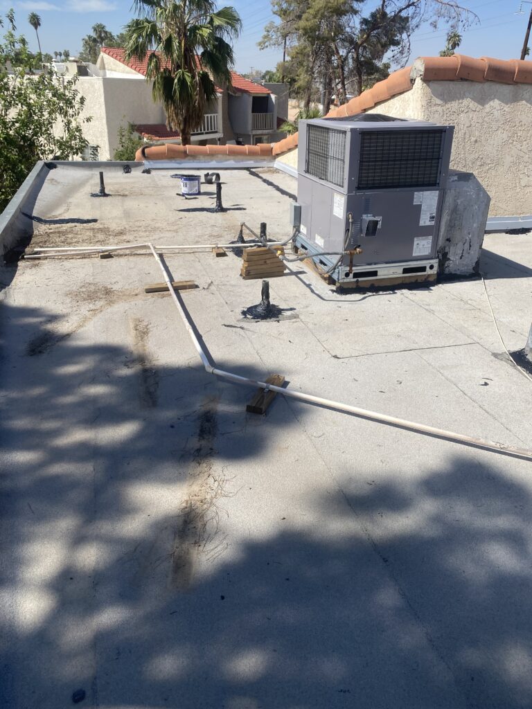 Low-slope roof with an HVAC unit, rooftop piping, vents, and parapet walls