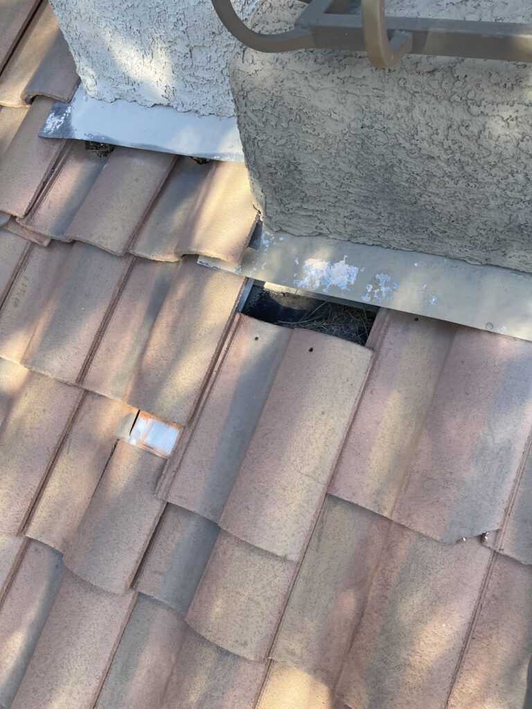 Metal flashing around a stucco chimney with a gap in the surrounding roof tiles