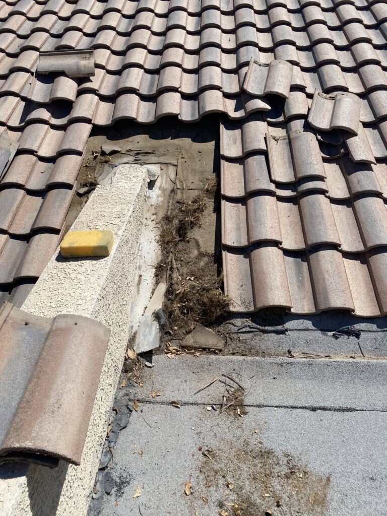 Removed roof tiles exposing wall flashing, roofing layers, and accumulated debris
