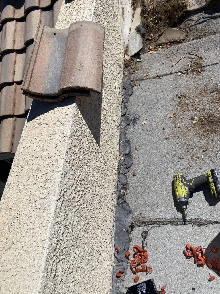 Exposed roofing beside a stucco wall with flashing, a drill, and roofing fasteners