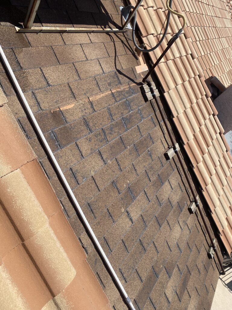 Brown asphalt shingle roof section beside curved tiles and rooftop piping