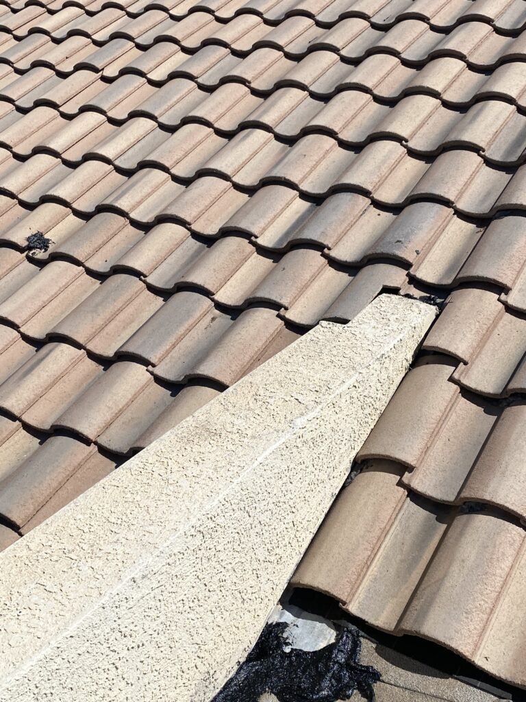 Curved roof tiles bordering a stucco wall with visible flashing and sealant