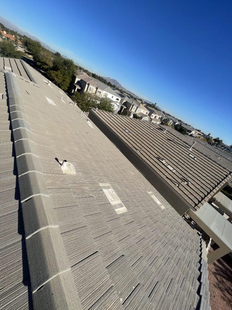 Gray tile roof slope with ridge caps, pipe flashing, and roof vents