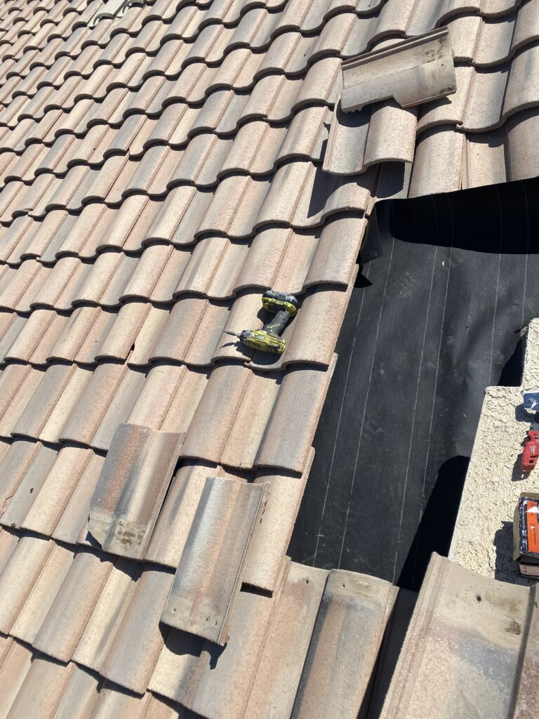 Roof tiles removed to expose black underlayment beside a stucco wall