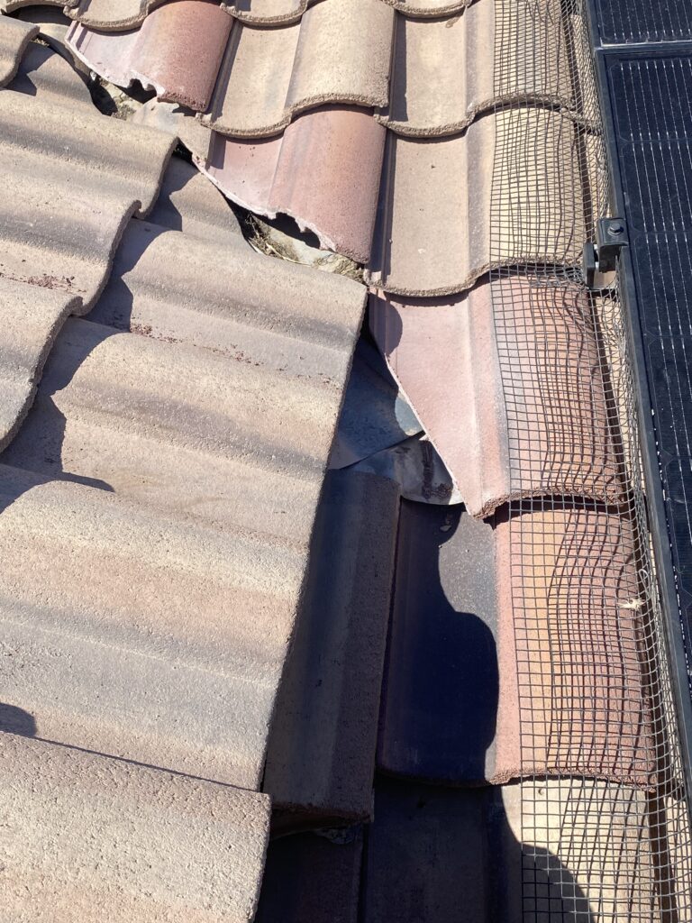 Tile roof valley with chipped tile edges beside solar panels and mesh